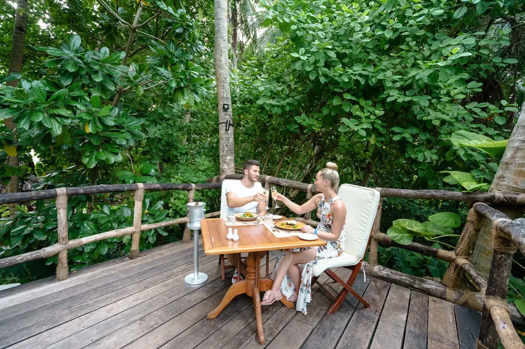 A couple enjoying a romantic outdoor meal amidst lush greenery, toasting with champagne.