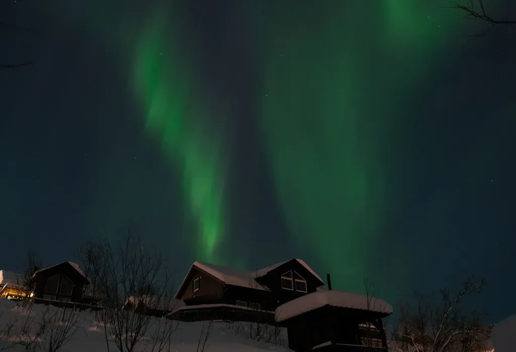 Breathtaking view of the Aurora Borealis illuminating snowy cabins in winter night.